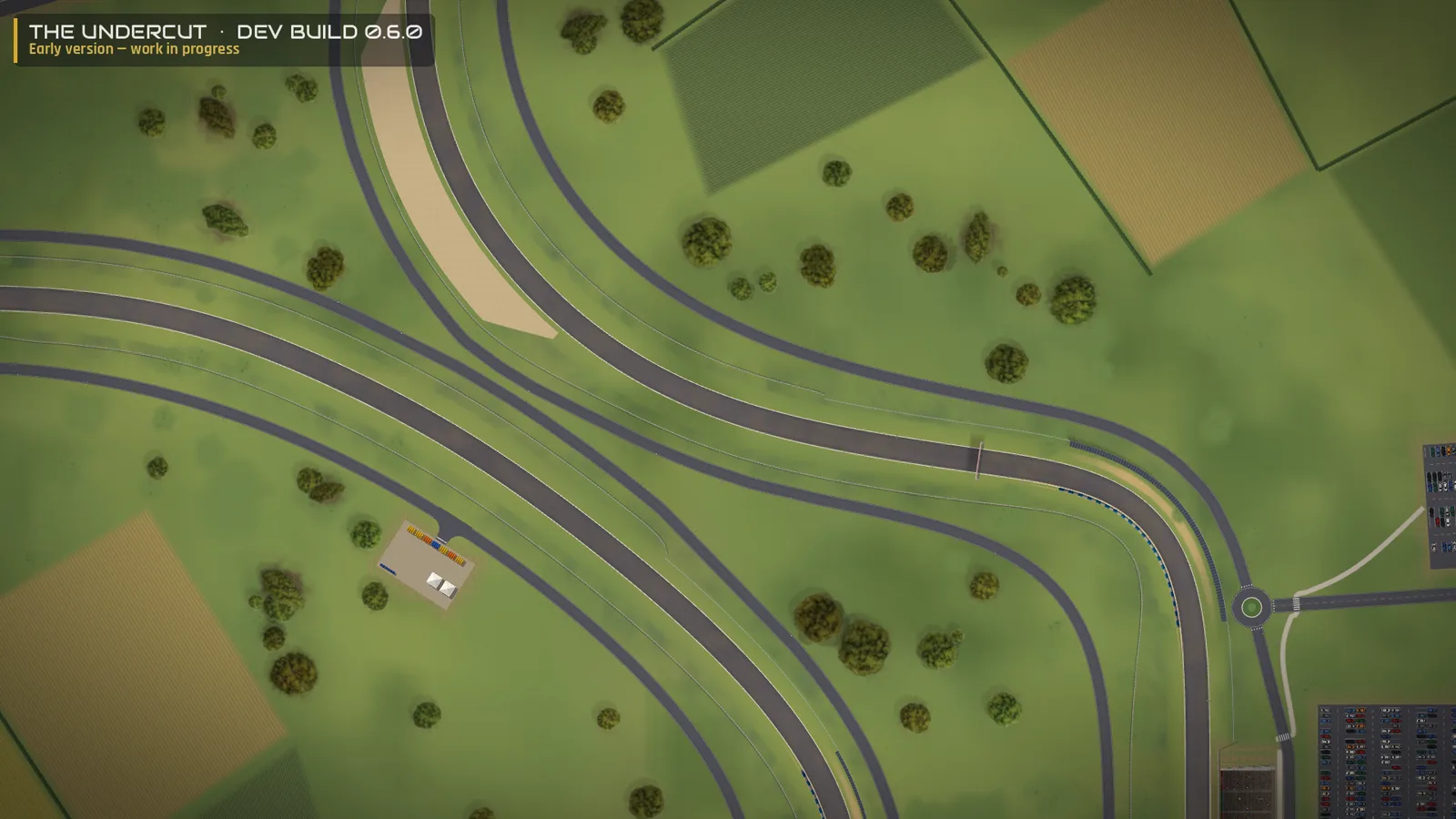 The Undercut, Entwicklungsversion 0.6.0 – Nahansicht: die Strecke mit Kiesbett, einer Notausfahrt, einer Servicestraße zu einem Kreisverkehr und einem Parkplatz, dahinter Felder